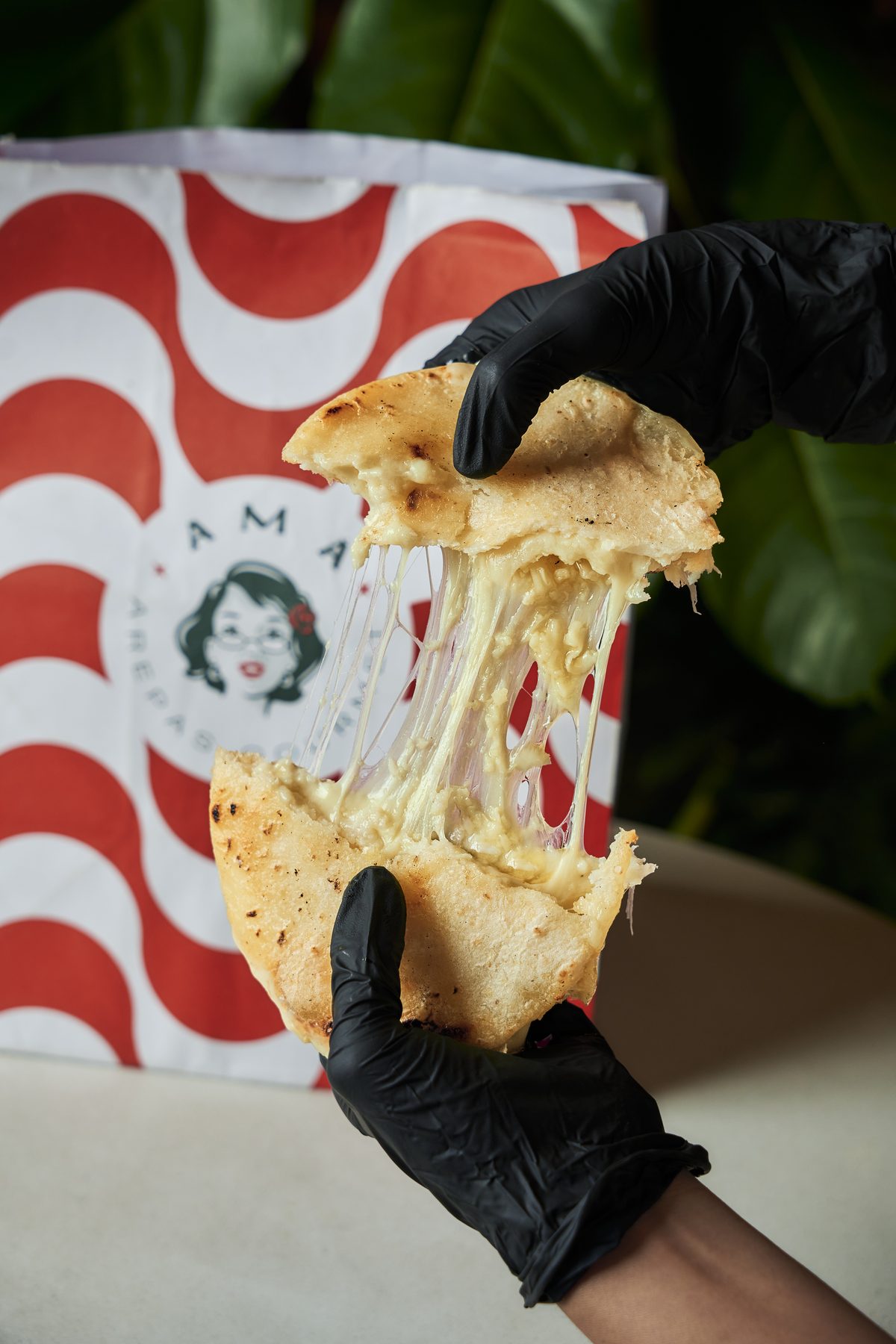Una arepa Amá recién partida con el queso derretido, frente a la bolsa de la marca